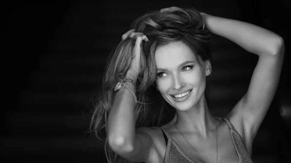 Black and white horizontal portrait of a woman in a grey dress. Professional make-up. Dark background