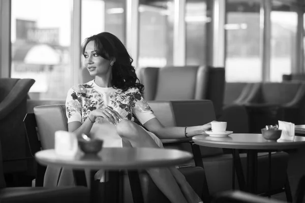 Молодая женщина пьет кофе и пользуется смартфоном, сидя в помещении городского кафе. Кафе городской образ жизни. Портрет красивой девушки. Черное и белое — стоковое фото