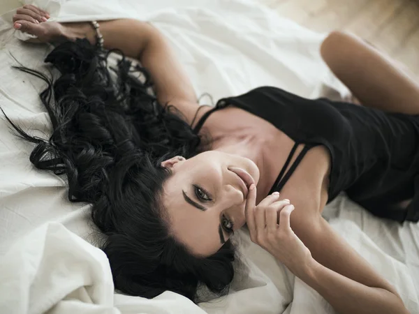 Primer plano de la joven sexy en lencería posando en la cama con hermosos ojos grises. Chica morena con ropa interior negra en su dormitorio — Foto de Stock