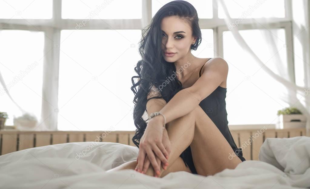 Close-up of sexy young woman in lingerie posing on the bed with beautiful grey eyes. Brunette girl with black underwear in her bedroom