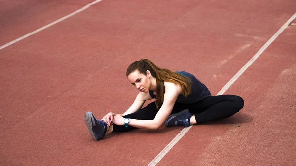 Mujer atlética estirando sus músculos antes de trotar en la pista — Foto de Stock