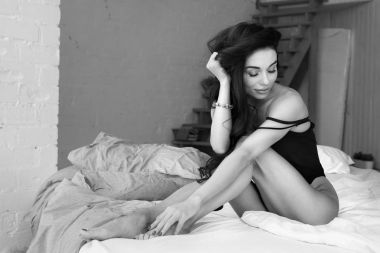 Çekici ve rahat baştan çıkarıcı genç kadın bağsız kıl ve ince gövde iç çamaşırı giyiyor sabah erkenden evde yatak beyaz çarşaf üzerinde yatıyor. Siyah beyaz resim.