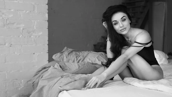 Attraktiva och avslappnad förförisk ung kvinna med lös hår och smal kropp bär underkläder liggande på vita lakan i sovrummet hemma tidigt på morgonen. Svart och vit bild. — Stockfoto