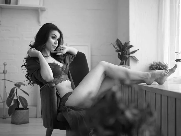 Sensuele vrouw zit naast het venster in lingerie in haar appartementen in de vroege ochtend. Zwarte ang wit foto. Oude hollywood-stijl. — Stockfoto