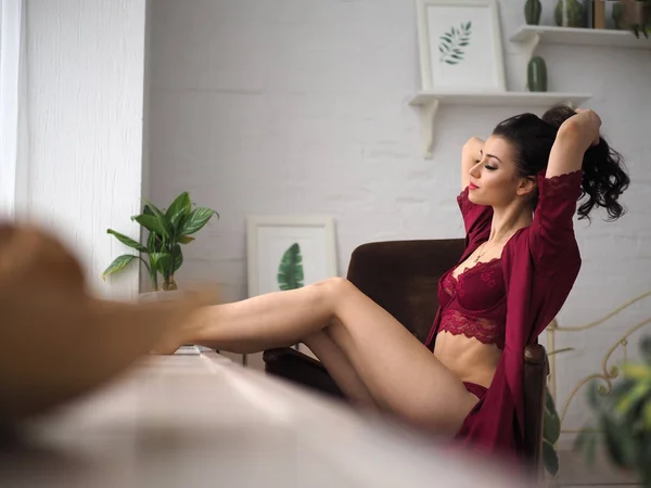 Bella e premurosa donna seduta sul bracciale in lingerie rossa accanto alla finestra. Risveglio sensuale . — Foto Stock