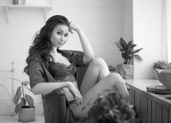 Donna sensuale siede accanto alla finestra in lingerie nei suoi appartamenti la mattina presto. Foto in bianco e nero. Vecchio stile hollywood. Lei guarda la macchina fotografica e sorride . — Foto Stock