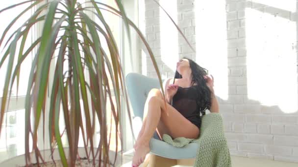 Seksowna brunetka siedzi na fotelu i rozciąganie wczesnym rankiem. Zmysłowy przebudzenia. Pokusa. — Wideo stockowe
