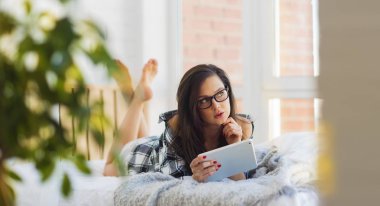 Bir yatakta yatarken bir güzel blogger yazar online bir tablet kullanarak bir makale yazıyor. Genç bir kız bir erkek gömlek çıplak bir vücut üzerinde