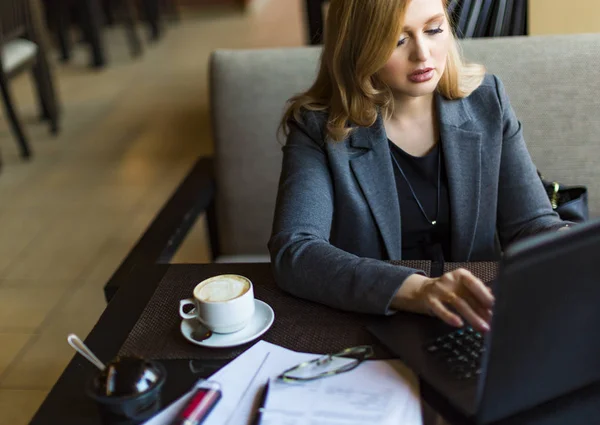 Empresária sentada em uma cafeteria à mesa de madeira, tomando café e usando laptop. Mulher navegando na internet, conversando, blogando . — Fotografia de Stock
