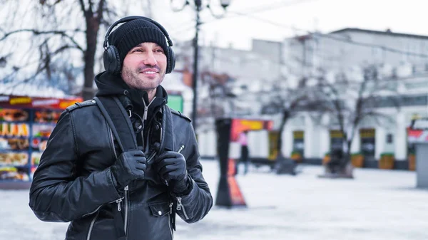 Χαμογελαστός άνθρωπος τουριστικά, με τα πόδια από την πόλη του χειμώνα και ακρόασης μουσικής μέσω ακουστικών — Φωτογραφία Αρχείου
