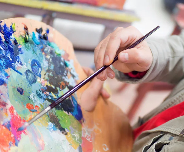 Primo piano della mano dell'uomo mescolare vernici con pennello in tavolozza e pittura nature morte quadro su tela in studio artista — Foto Stock