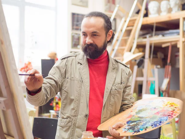 Ontworpen door kunstenaar man afwerking houdt zijn meesterwerk een penseel in de hand — Stockfoto