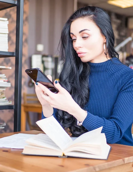 Όμορφη γυναίκα στην καφετέρια. Πρόσωπο σε πλάγια όψη, στείλτε μήνυμα από smartphone. Φοιτητής ανάγνωση βιβλίων για τις εξετάσεις στη βιβλιοθήκη, κρατώντας το κινητό τηλέφωνο. — Φωτογραφία Αρχείου