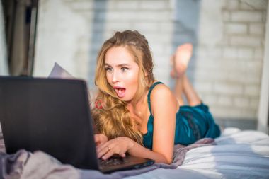 Genç kadın şaşkınlık. Onu laptop izlerken yatakta yalan söylüyor. Çapraz vintage bir görünüm ile görüntü işleme.