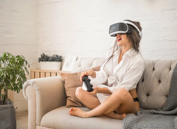 Excited young woman in VR goggles driving car in virtual reality. Lady screaming when turning virtual steering wheel, teen playing in racing computer game or road simulator, enjoying 3d gaming at home