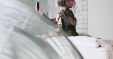 Kadın eğlenceli olması onun pijamaları yatağın üstüne oturan ve müzik. Cep telefonu şarkıları dinlerken Güzellik