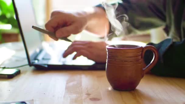 关闭在笔记本电脑上工作的匿名人的手与一杯热茶 专注于杯热茶 — 图库视频影像