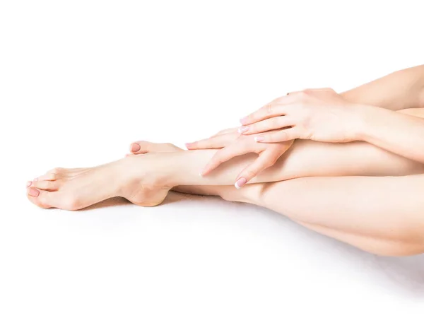 Gros plan d'une femme qui applique une crème hydratante sur sa jambe et ses pieds. Pieds et mains de beauté isolés sur fond blanc. Jeune femme touchant les mains et les jambes avec des ongles français soignés — Photo