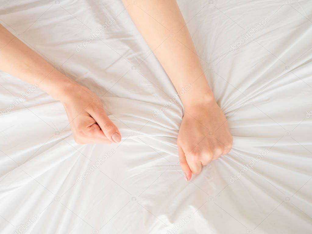Female hands clutching bedsheets.