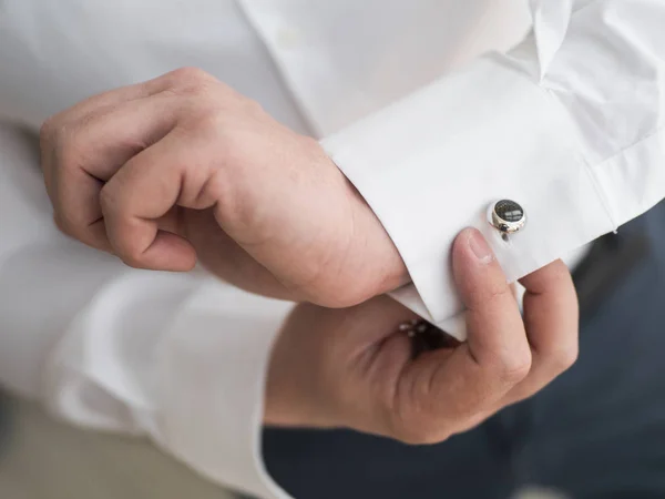 A man wears buttons of cufflinks on the sleeves of the white shirt. Businessman getting dressed by the window.