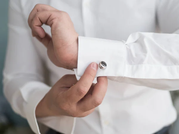 A man wears buttons of cufflinks on the sleeves of the white shirt. Businessman getting dressed by the window.