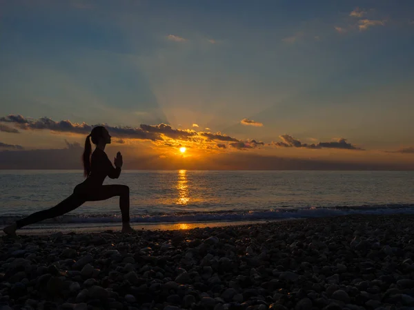 Mulher fazendo exercício de ioga durante o pôr do sol na praia . — Fotografia de Stock