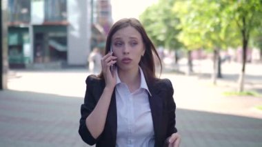 Ciddi bir iş kadını sokakta yürürken telefonla konuşuyor.