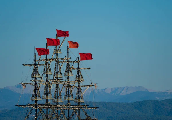 Foto de altos mastros de madeira de navios antigos no porto contra o céu azul e montanhas à noite — Fotografia de Stock