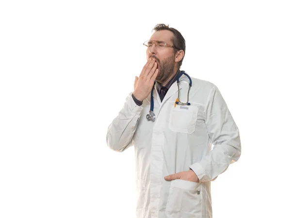 男医生戴听诊器，戴在白色背景上，厌烦地打呵欠，用手捂住疲惫的嘴. — 图库照片
