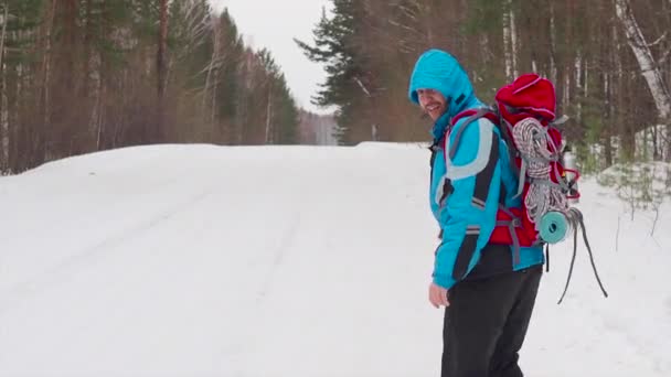 Back view of a hitchhiker man on the winter road. walking and try to stop a car. — Stockvideo