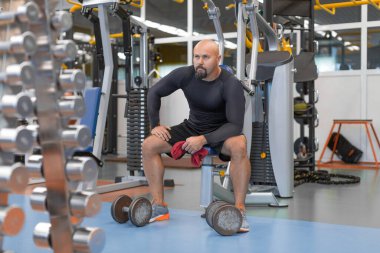 Egzersizden sonra orta yaşlı yorgun bir adam spor salonunda dinleniyor. Sağlık ve Spor Konsepti.