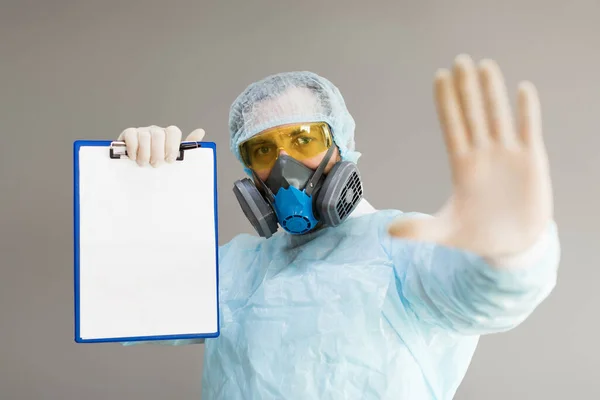 En läkare i respirator och skyddskläder visar en stoppskylt med handflatan och håller ett papper med en diagnos — Stockfoto