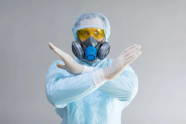 Doctor in protective clothing with crossed arms shows stop gesture.