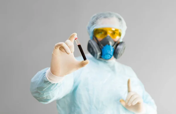 Zdjęcie lekarza w ubraniu ochronnym trzyma probówkę z próbką zakażonej krwi w ręce i pokazuje znak uwagi palcem.. — Zdjęcie stockowe