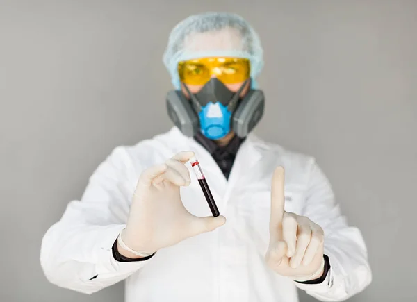 A doctor in protective clothing holds a test tube with a sample of infected blood in his hand and showing attention sign by finger. — Stock Photo, Image