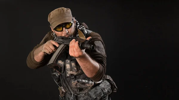A mercenary with a gun aims at the enemy. Close-up on a dark background. — Stock Photo, Image