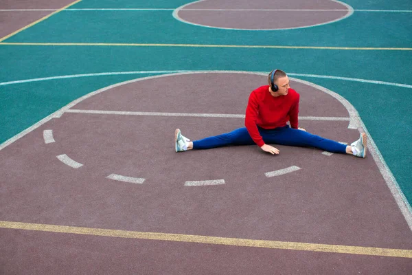 Genç bir adam spor sahasında antrenmandan sonra bacaklarının kaslarını esnetir.. — Stok fotoğraf