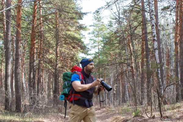 Bird watcher walks through the woods with a camera.