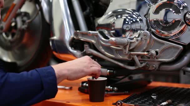 El hombre agita el café con una llave inglesa cerca de la motocicleta en un taller. — Vídeo de stock