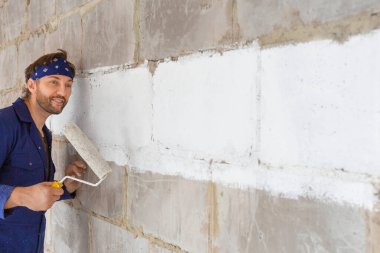 Adam duvarı boyuyor. İş üniformalı bir inşaatçı..