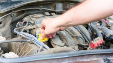 Erkek el motor dolgusunu açar ve arabanın motoruna yağ döker.