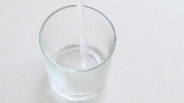 Water wordt in een glas gegoten en een bruisende aspirinetablet valt in het water. Uitzicht vanaf de bovenkant. — Stockvideo