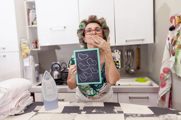 Mature housewife woman with curlers shows a board with hearts — Stock Photo, Image