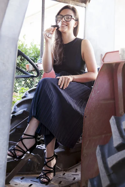 Bella giovane donna seduta su un trattore in possesso di un bicchiere di wi — Foto Stock