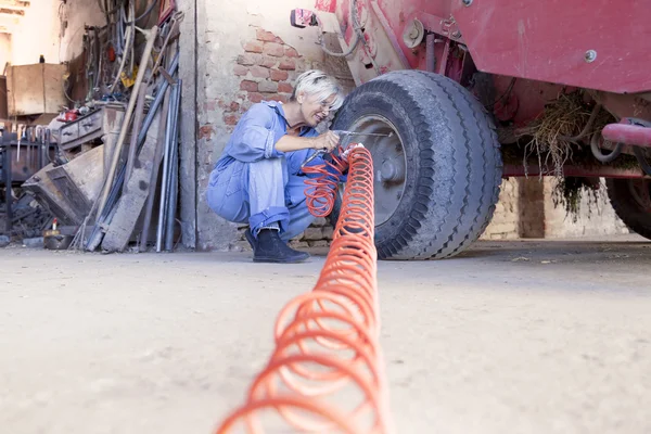 Mechanical mature female inflates the tire of the tractor — Stock fotografie