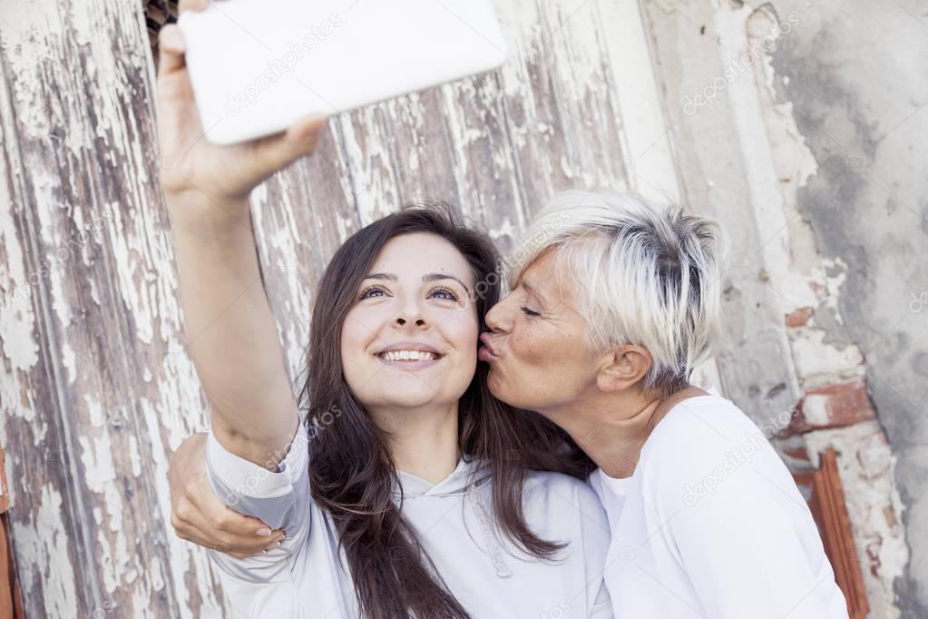 mother and adult daughter take a selfie outdoors