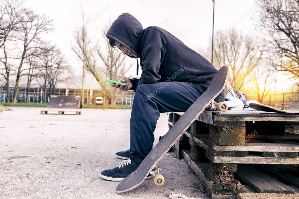 sitting young adult skateboarder writes a message on smart phone