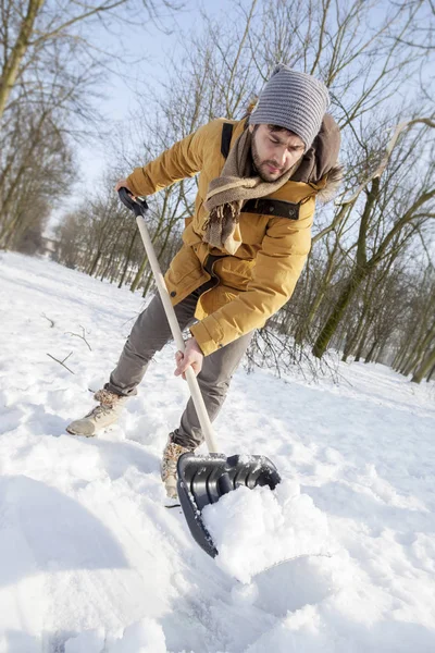 Jonge man sneeuwschuiven in de buurt van een kleine hout — Stockfoto