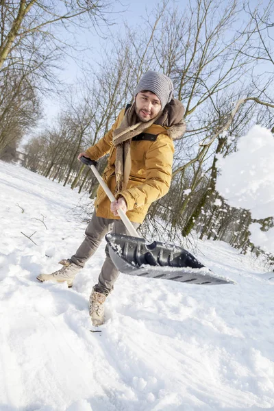 Ung man skotta snö nära en liten trä — Stockfoto