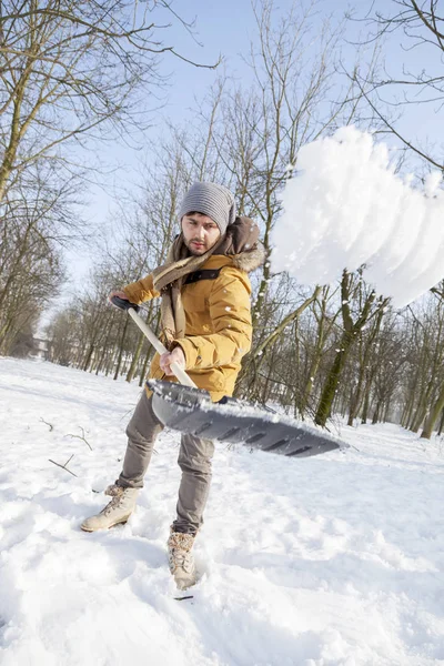 Ung man skotta snö nära en liten trä — Stockfoto